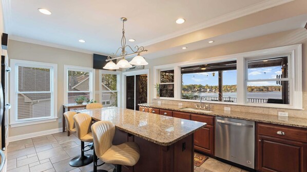 A modern kitchen with a large island, stainless steel appliances, and large windows offering views of a lake and trees. - Lake Norman Retreat w/ Pool, Hot Tub & Private Dock Lake Life Cove by Avantstay (Mooresville)