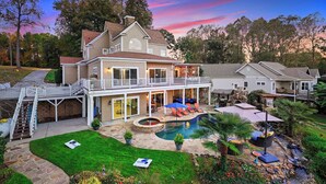 Una casa de dos pisos con piscina, mobiliario exterior y un porche cubierto.