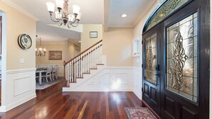 Un vestíbulo espacioso con una escalera de madera, un comedor y una puerta de vidrio decorativa.