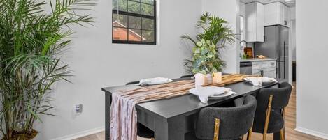 A modern dining area with a black table, four chairs, and a potted plant.