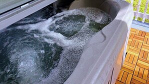 Ein Whirlpool mit fließendem Wasser, umgeben von einer Holzterrasse und einem weißen Zaun.