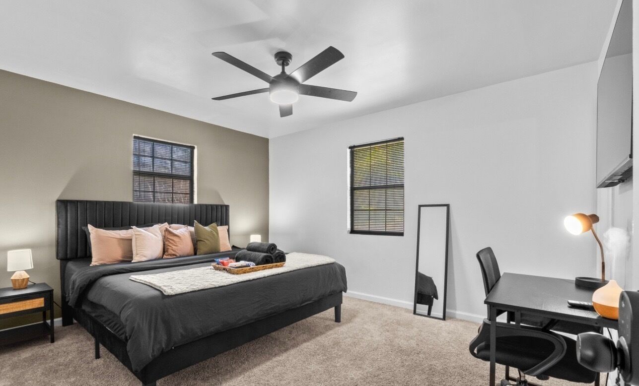 A modern bedroom with a bed, bedside table, lamp, and a desk with a chair.
