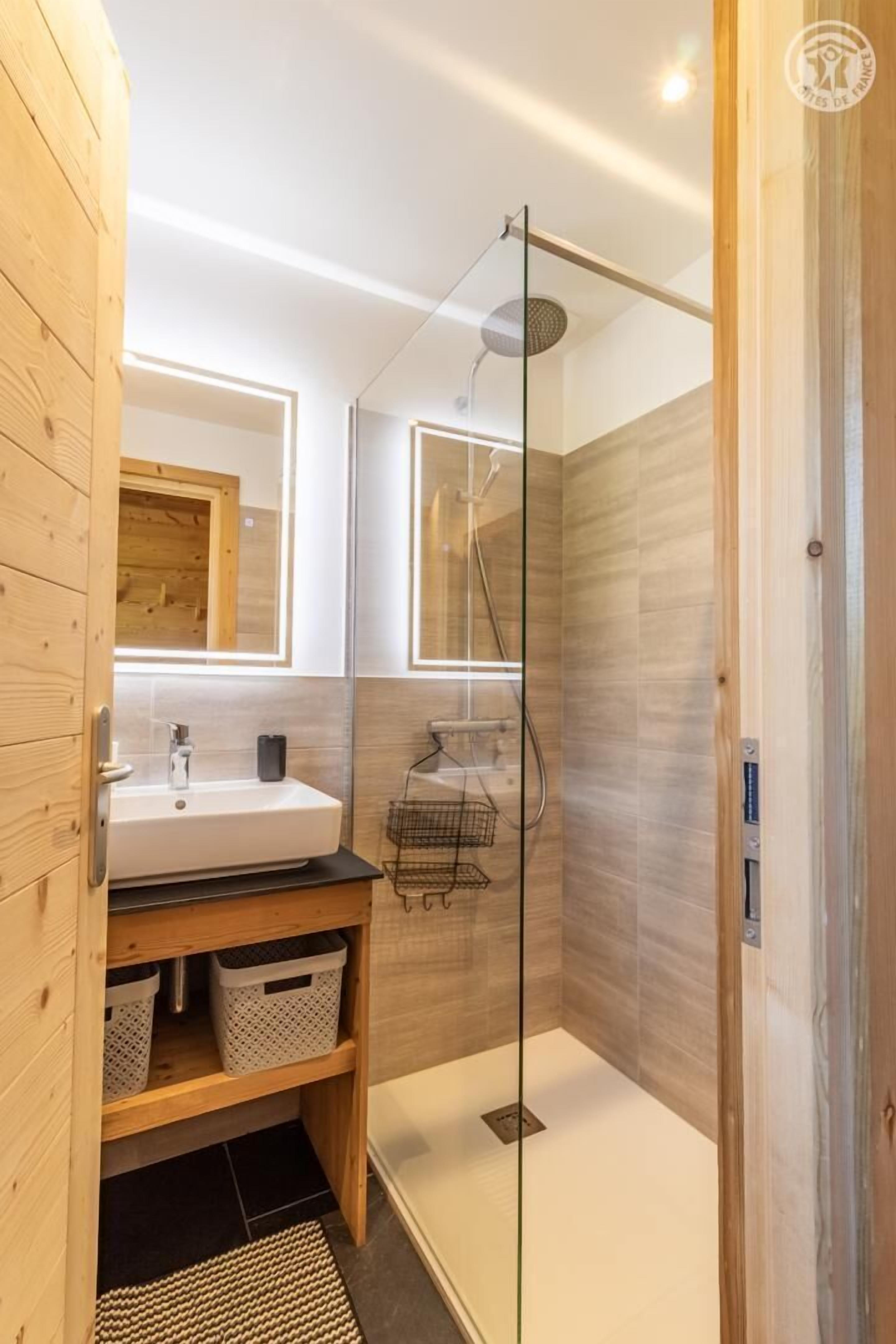 Un baño moderno con ducha de vidrio, tocador de madera y un espejo grande.