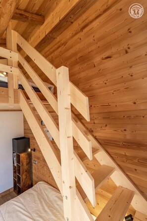 Eine Holztreppe führt zu einer erhöhten Ebene mit einem Bett und einem kleinen Tisch.