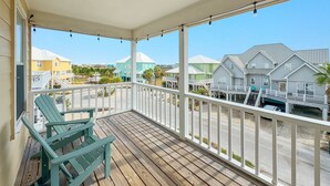 Una terraza de madera con barandilla blanca, dos sillas Adirondack verdes y vista a casas coloridas al fondo.