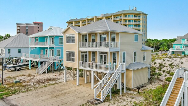 Una propiedad frente a la playa con varias construcciones, incluyendo una casa de dos pisos con balcón y un edificio más grande con múltiples balcones.