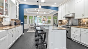 A modern kitchen with white cabinets, a central island with stools, a stove, and a view of greenery through large windows. - Experience luxury at Thorne Swift Lakehouse, Harbor Springs - Lake Michigan (Harbor Springs)