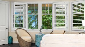 A bedroom with a large bed, two windows with white shutters, a chair, a small table, and a potted plant. - Experience luxury at Thorne Swift Lakehouse, Harbor Springs - Lake Michigan (Harbor Springs)