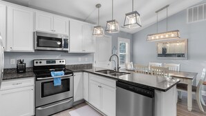 Una cocina moderna con armarios blancos, electrodomésticos de acero inoxidable, encimera de granito e iluminación colgante.