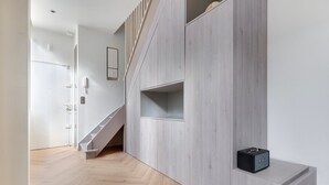 Un interior moderno con una escalera de madera, estanterías empotradas y un pequeño altavoz negro sobre una repisa.
