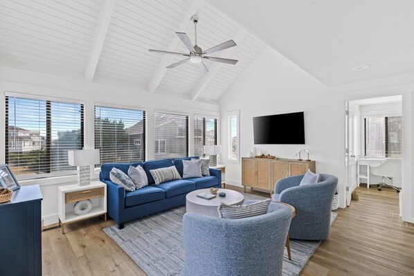 A modern living room with a blue sofa, two armchairs, a TV, and a ceiling fan. - Escape to Sandy Dreams, a beautifully remodeled villa perfectly situated on Bald Head Island. (Bald Head Island)