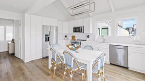 Una cocina moderna con armarios blancos, un refrigerador de acero inoxidable, un microondas y un lavavajillas. Hay una mesa de comedor con cuatro sillas y una ventana que proporciona luz natural.