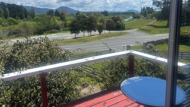 Un balcón con vista a una carretera, vegetación y una montaña al fondo.