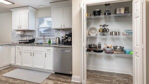 A kitchen with white cabinets, a dishwasher, and a built-in pantry with shelves. - Serene Sunshine State Escape (Deltona)