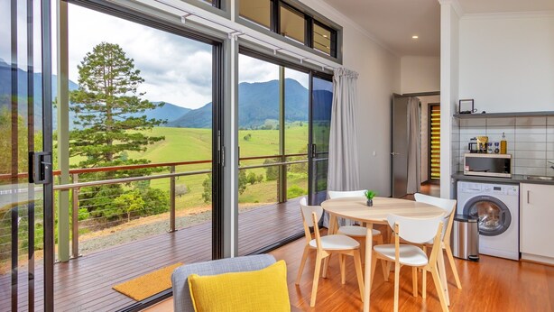 Moderni keittiö, josta avautuu näkymä vuoristomaisemaan, ruokailutila pöytineen ja tuoleineen sekä suuri liukuovi, joka johtaa ulkoterasille.