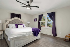 Quarto com cama, ventilador de teto, janela com cortinas e vista para o exterior.