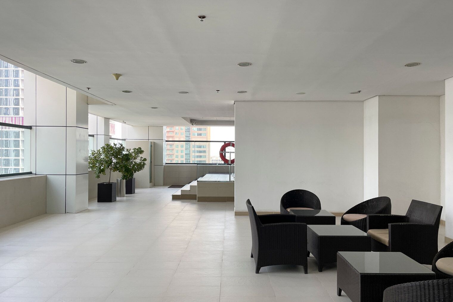 Un salon spacieux et moderne, doté d’une grande fenêtre, de meubles en rotin noir et d’une plante en pot.