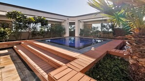 A modern outdoor swimming pool with wooden deck seating and surrounding greenery. - Blueground | DIFC, rooftop pool, nr Burj Khalifa (Dubai)