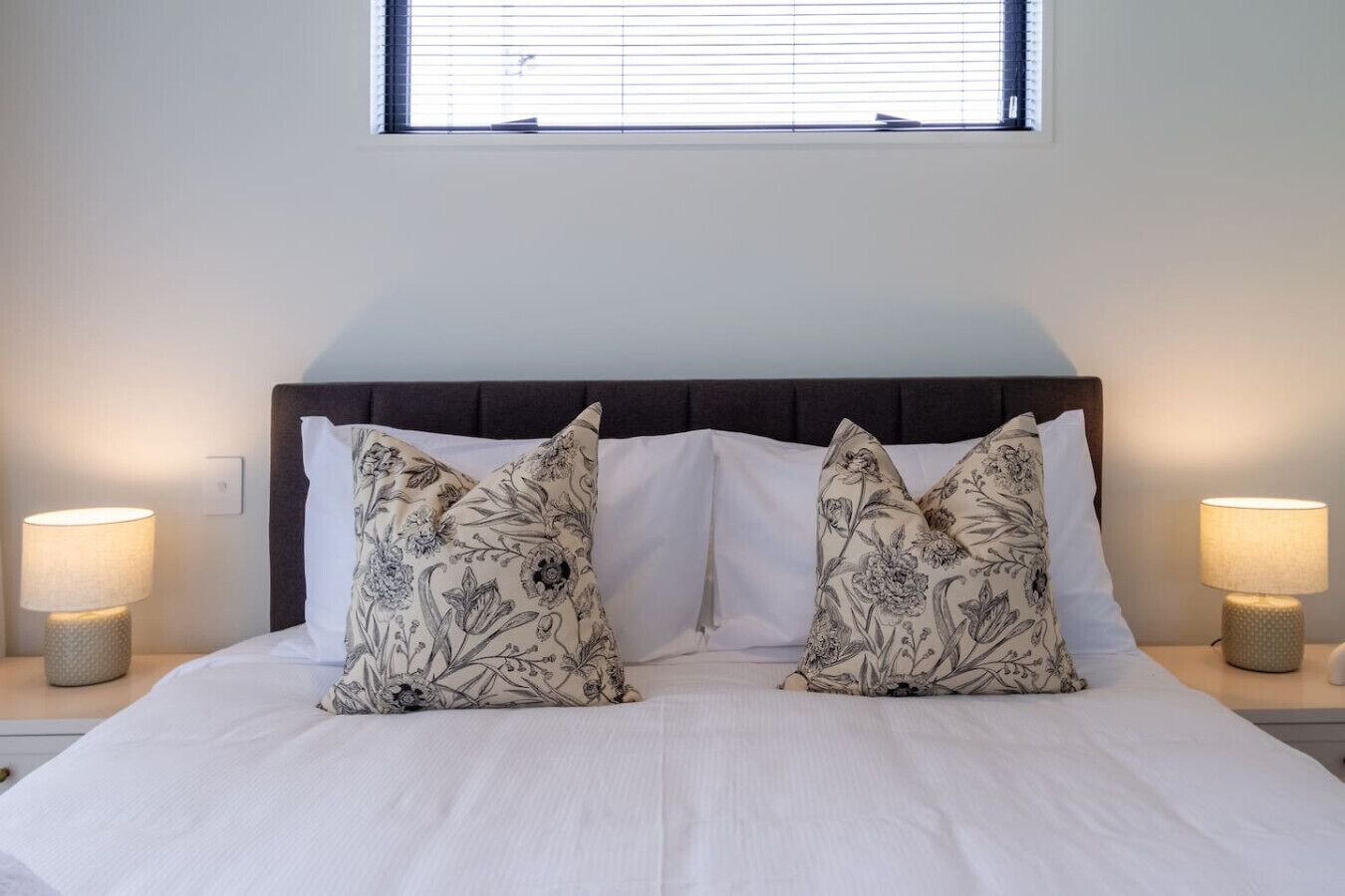 A neatly made bed with two pillows, a headboard, and two bedside lamps.