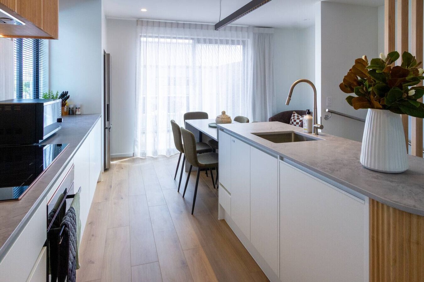 Une cuisine moderne dotée d’un îlot central, d’un coin repas avec des chaises et d’une grande fenêtre agrémentée de rideaux légers.