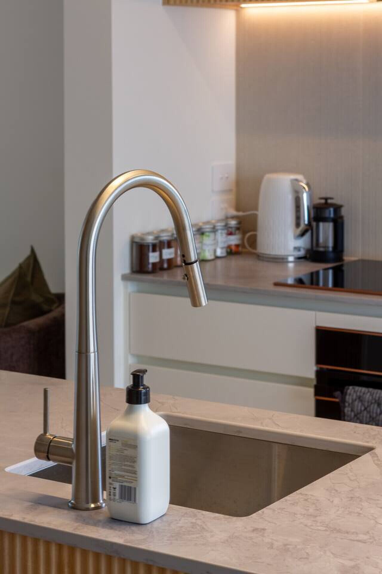 A modern kitchen with a stainless steel faucet, a coffee maker, and a bottle of hand soap on the counter.