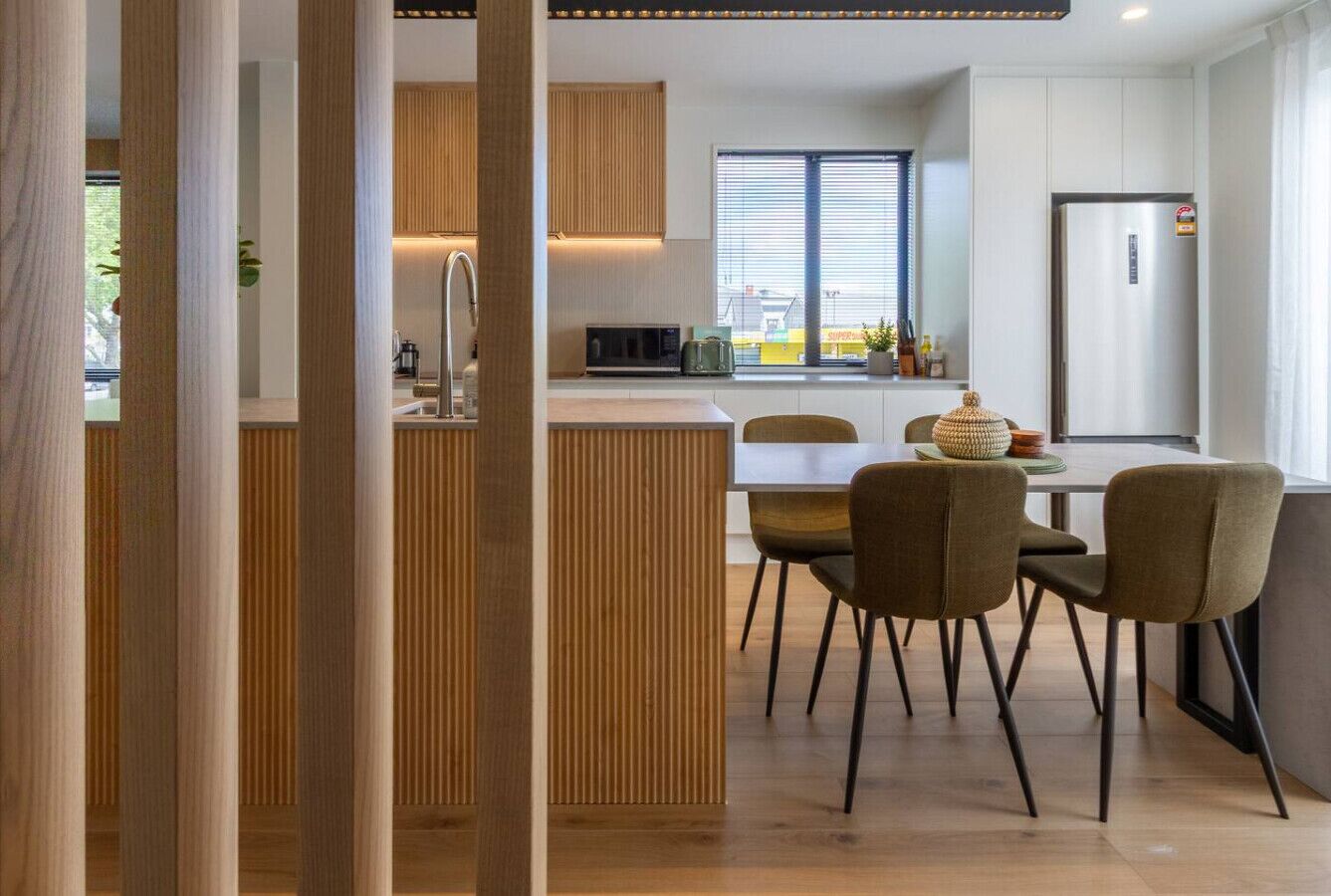 Una cocina moderna con una isla central, paneles de madera y un comedor con sillas y una mesa.