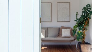 Un salon moderne avec un canapé beige, deux œuvres d’art encadrées et une grande plante en pot.