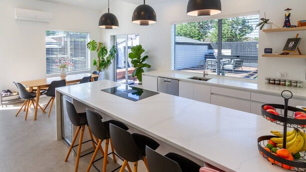 Une cuisine moderne avec un îlot central, des suspensions noires et un panier de fruits.