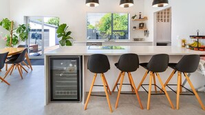 Une cuisine moderne dotée d’un îlot central, de tabourets de bar noirs et de luminaires suspendus.