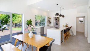 Une cuisine moderne dotée d’un îlot central, d’un coin repas avec des bancs et offrant une vue sur un jardin grâce à de grandes fenêtres.