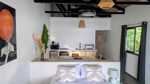 A modern bedroom with a bed, bedside table, and a view of a kitchen area. - Brisas del Mar Bocas (Bastimentos)