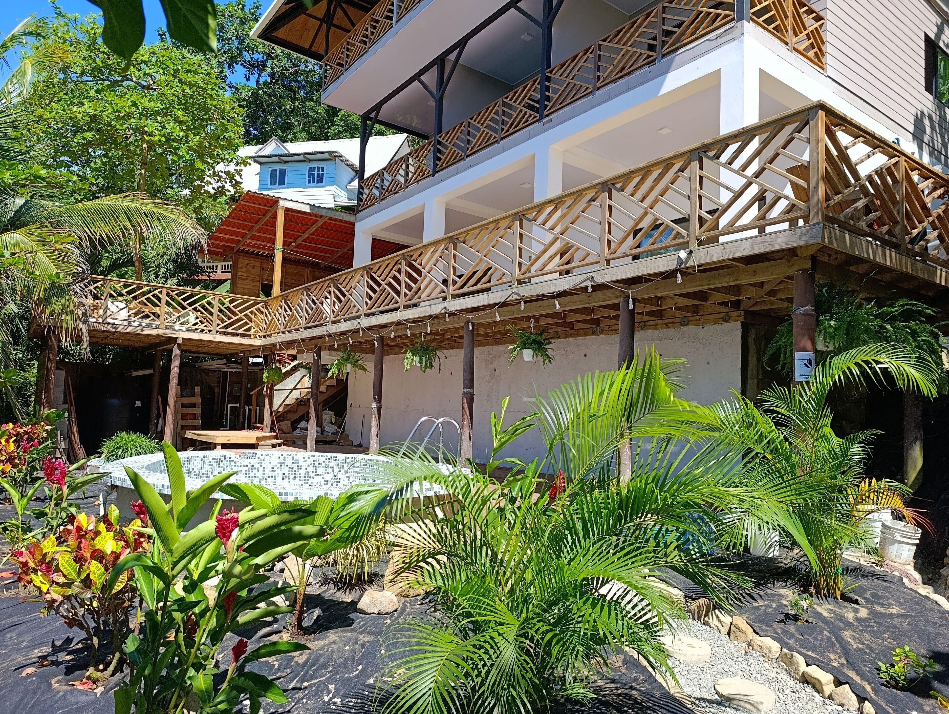 Un edificio moderno con un área exterior techada, piscina y exuberante vegetación tropical.