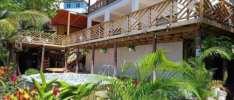 Un edificio moderno con un área exterior techada, piscina y exuberante vegetación tropical.