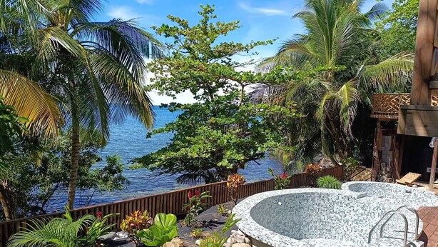 A hot tub surrounded by tropical plants and a wooden deck, overlooking a body of water. - Brisas del Mar Bocas (Bastimentos)
