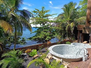 A hot tub surrounded by tropical plants and a wooden deck, overlooking a body of water. - Brisas del Mar Bocas (Bastimentos)