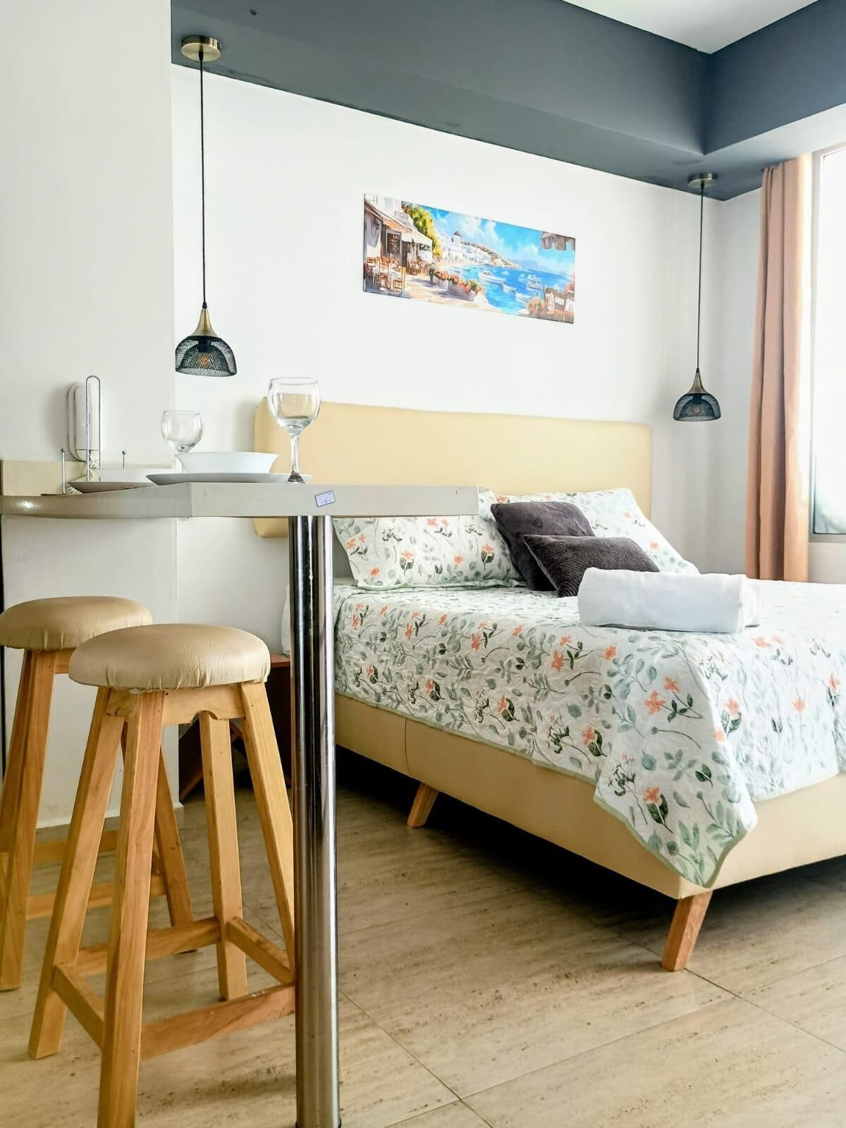 Un dormitorio con una cama, dos taburetes de madera, un escritorio y un cuadro en la pared.