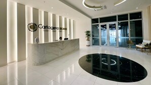 Een moderne hotellobby met een receptiebalie, een brede glazen ingang en een rond, reflecterend vloerelement.