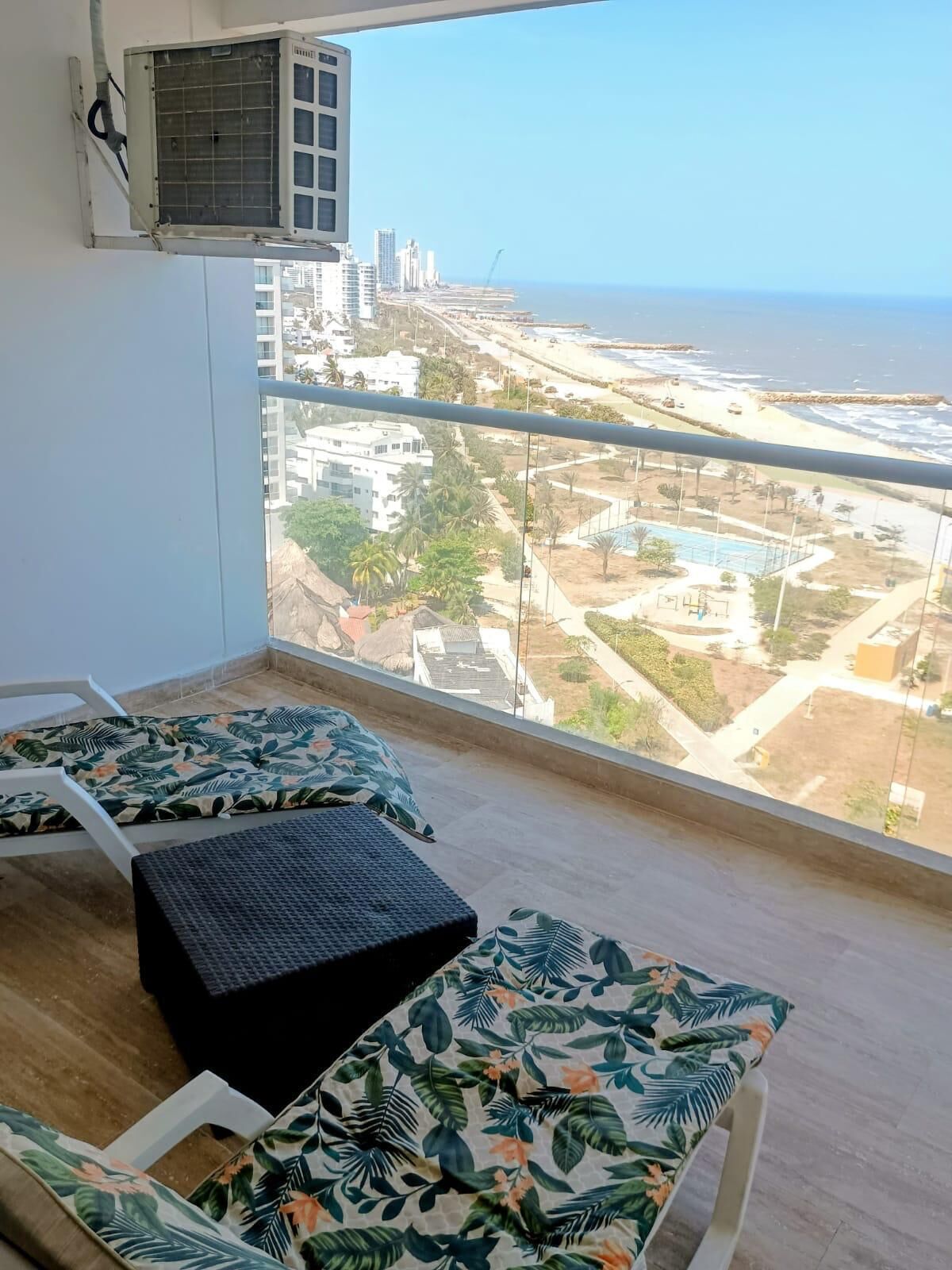 A balcony with a view of a beach and cityscape, featuring two lounge chairs and a small table.