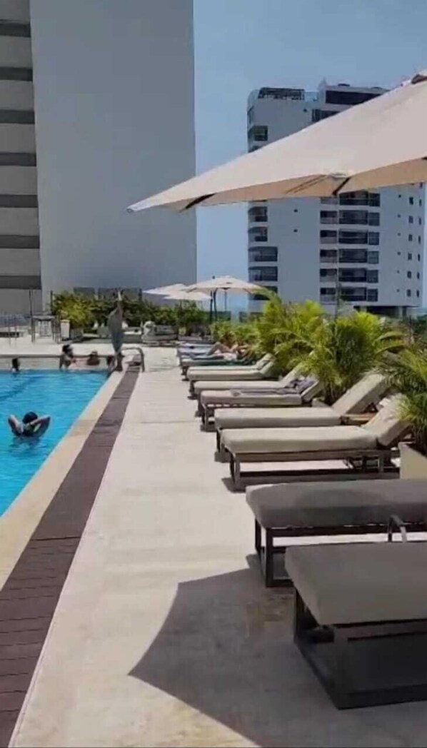 A swimming pool with lounge chairs and umbrellas, surrounded by tall buildings. - Suite vacacional (Cartagena)