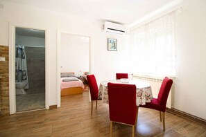 Una habitació amb un llit, una taula petita amb cadires, un radiador i una finestra amb cortines.