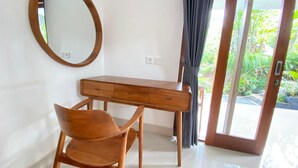 Una habitación con un escritorio de madera, una silla, un espejo redondo y un ventanal corredero que da a un jardín.