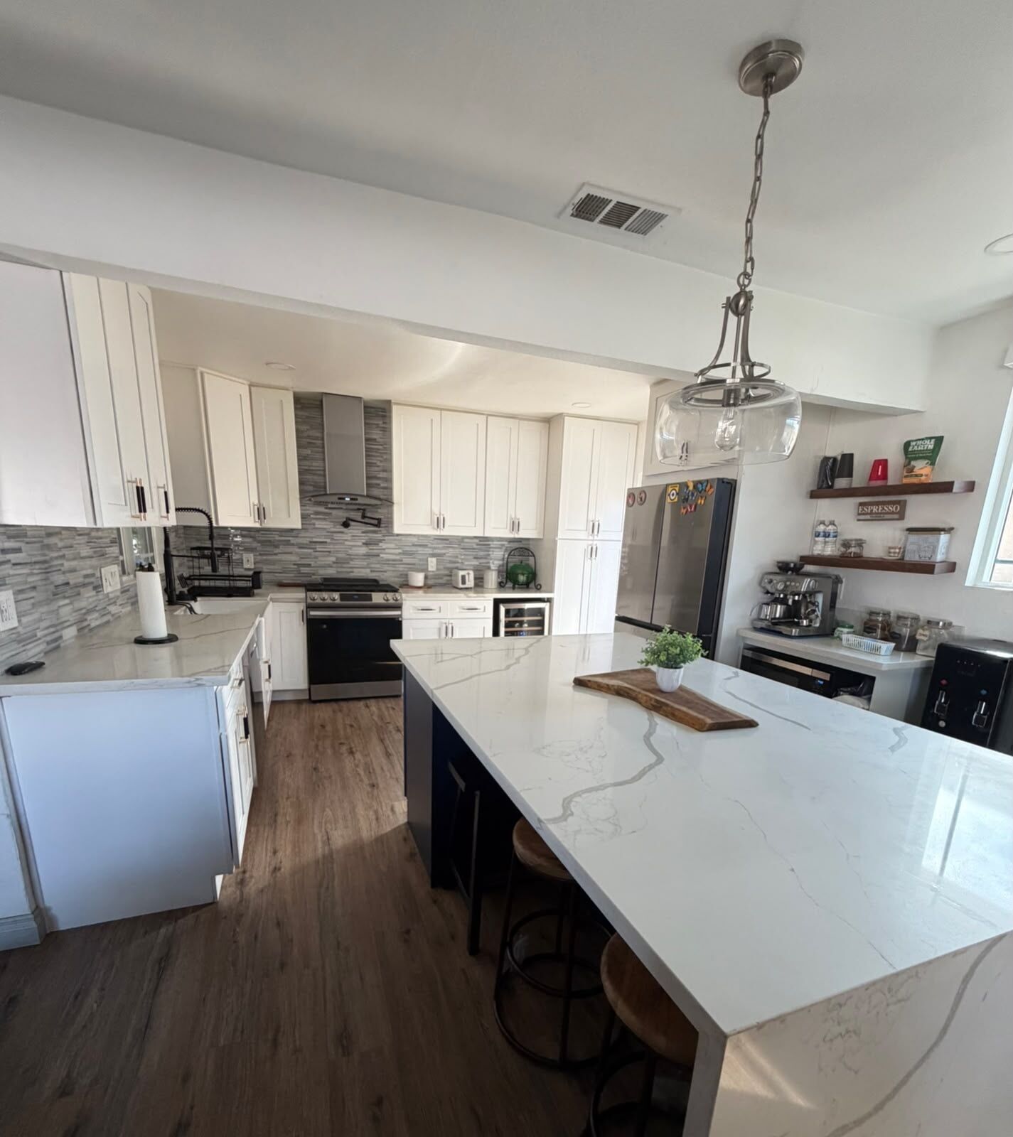 A modern kitchen with white cabinetry, a marble island, and stainless steel appliances.