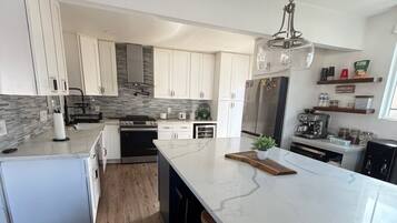 A modern kitchen with white cabinetry, a marble island, and stainless steel appliances.