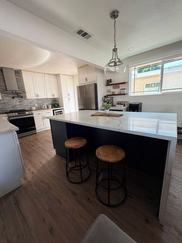 A modern kitchen with a central island, stainless steel appliances, and wooden stools.