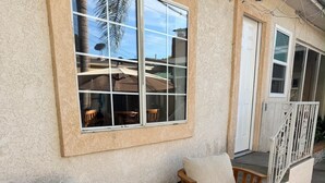 Eine Terrassenfläche mit zwei Holzstühlen, einem kleinen runden Tisch, einer weißen Tür und einem Geländer.