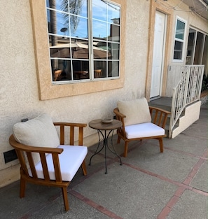 Un patio con dos sillas de madera y una pequeña mesa redonda, una puerta blanca y una barandilla.