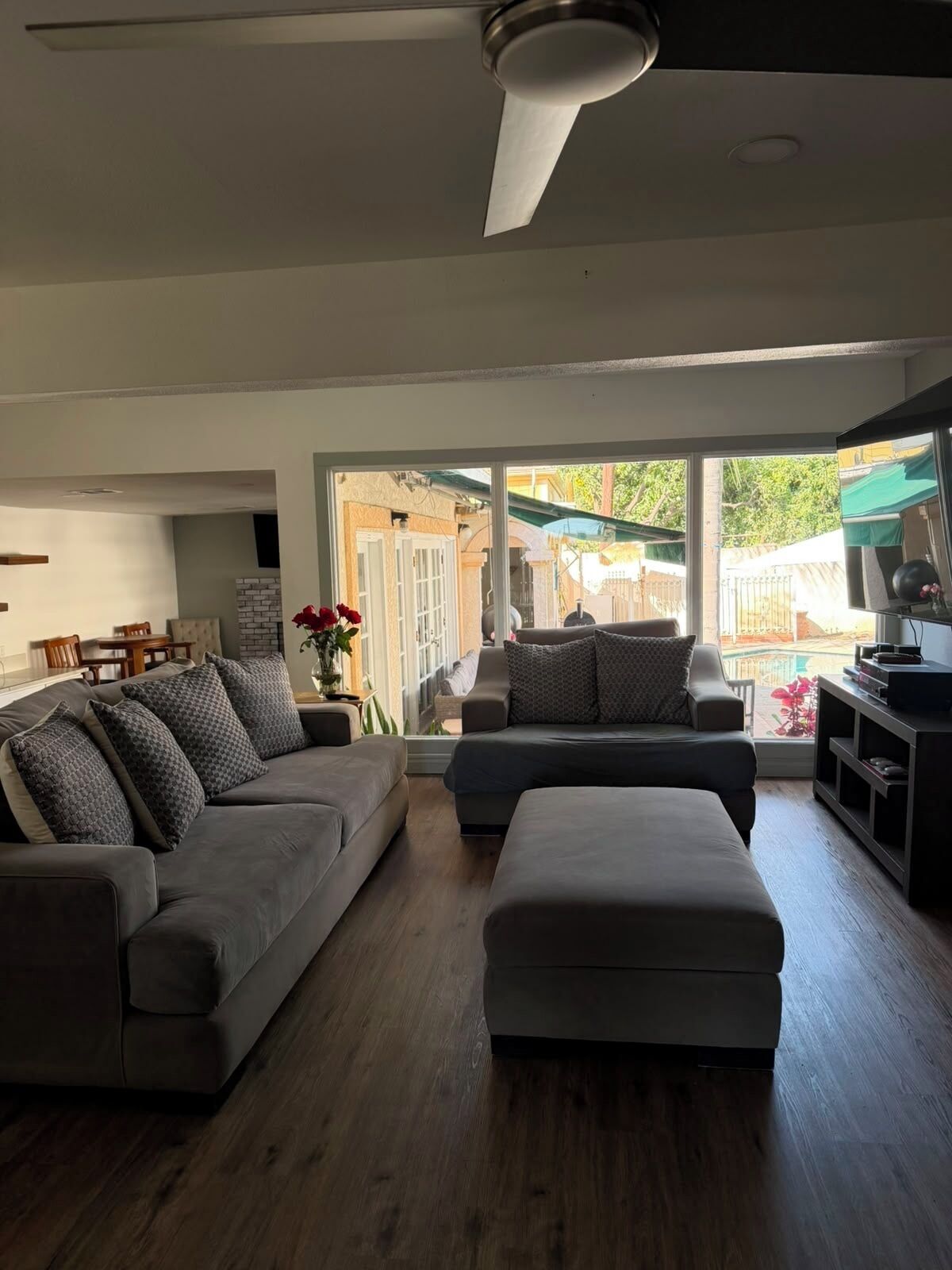 A modern living room with a grey sectional sofa, an ottoman, and a dining area with wooden furniture.