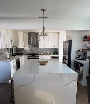 Una cocina moderna con muebles blancos, una isla grande de mármol y electrodomésticos de acero inoxidable.
