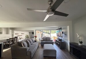 A modern living room with a sofa, ottoman, and a ceiling fan.