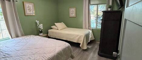 Une chambre avec deux lits, un ventilateur de plafond, une fenêtre avec des rideaux et un tapis à carreaux.